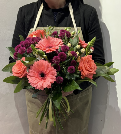Coral Burst by Octagon Flowers Bolton - A vibrant hand-tied bouquet featuring bold coral gerberas, raspberry chrysanthemums and fresh coral roses, with soft cream accents and lush greenery.